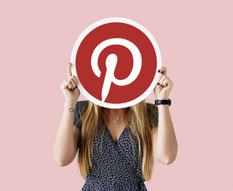 junge Frau hält sich Pinterest-logo vor das gesicht