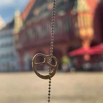 Entdecke einzigartige Souvenirs aus Stuttgart: Brezel Schmuck & Accessoires, inspiriert von schwäbischer Tradition. Die zarte Brezel-Kette ist fotografiert am Marktplatz in Freiburg.