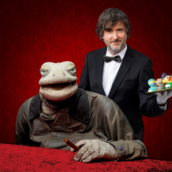 Michael Hatzius mit Echsenpuppe vor rotem Grund
