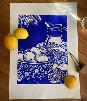 Linoldruck in einem lebendigen Blau der eine Schale voll Zitronen und einen Krug Limonade zeigt