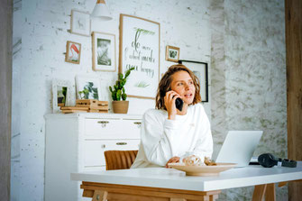 Frau beim Telefonieren vor ihrem Laptop
