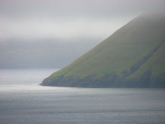 Ein steil in den Atlantik abfallender Küstenbereich. Er ist von dichtem Nebel verhangen. Das Wasser des Atlantiks schimmert in grauer Farbe.