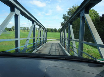 Von innen durch die Windschutzscheibe fotografiert die schmalste Autobrücke. Man sieht das Armaturenbrett und draußen die Metallträger der Brücke und das Gitterrost, über das man fährt. Es sieht aus, als wäre das Auto breiter als die Durchfahrt.