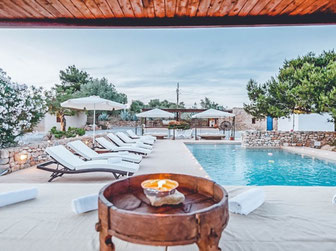 Swiming pool in Ibiza, blue sky and pine trees with a cozy brown, wooden Bali bed