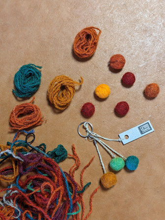 Plan de travail avec les fils de la laine de toute couleur mélangés, les balles en laine feutrée et un porte-clé avec trois petites pelotes de feutre - bleue, verte et marronne. 