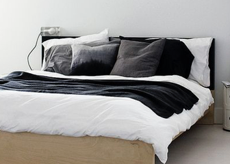 Doppelbett mit grauen und schwarzen Kissen und schwarzer Decke über ein weisses Duvet