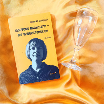 Buch "Ingeborg Bachmann - Die Widerspenstige" und ein Sektglas auf einem gelben Tuch