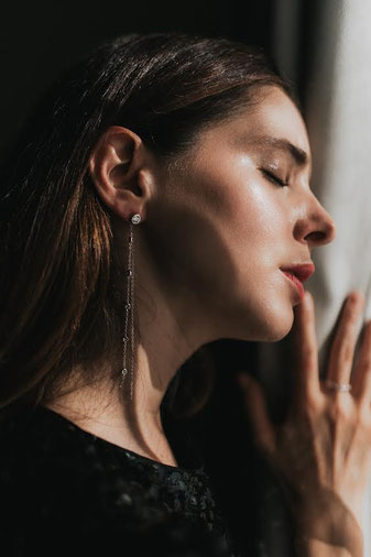 Side portrait of a woman with closed eyes in warm light. Long delicate silver earring and simple ring in focus, creating a calm and elegant atmosphere.