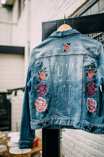 sportieve spijkerjasjes met bloemen en tekst voor bruid over trouwjurk buiten trouwen