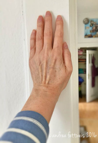 Dehnen des Schultergelenks vor dem Körper funktioniert leichter, wenn man die Hand zwischendurch gegen die Wand presst.
