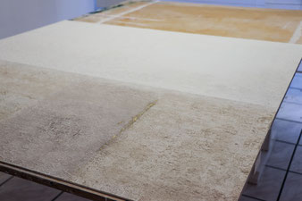 Arbeitstisch in der Werkstatt mit Werkstück: Eine Tafel 140 mal 140 bearbeitet mit Sand und Acrylfarbe in Naturtönen.