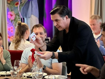 Romi, magicien à Toulouse, effectue un tour de close-up à table pendant un repas d’entreprise, sous les yeux des invités.