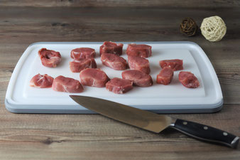 Fleisch mit dem Kochmesser auf dem großen Schneidebrett mit Saftrillen in Medaillons schneiden
