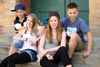 zwei Mädchen und zwei Jungen sitzen locker zusammen auf Treppenstufen