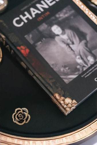 Chanel photo book on a black tray with gold detailing. Next to it lies a gold rose emblem, creating an elegant and luxurious scene.