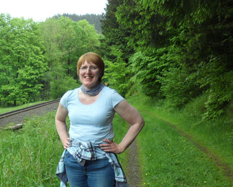 Ich stehe auf einem Weg neben Bahngleisen. Um mich herum grünes Gras und leuchtend grüne Laubbäume. Ich habe kurzes, kastanienbraunes Haar, trage ein hellblaues T-Shirt und Jeans, um die Hüften ein hellblau kariertes Baumwollhemd geknotet. 