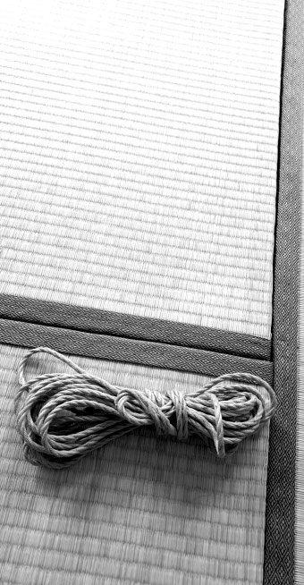 Schwarz-weiß-Stillleben eines zusammengelegten Juteseils für Shibari Bondage auf einer Tatamimatte.