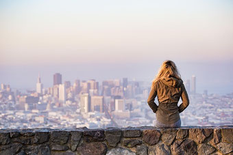Sitzende Frau auf der Steinmauer mit Blick auf die Stadt denkt über neue Wege nach