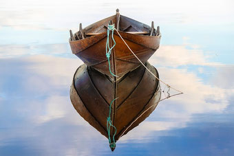 Kleines Holzboot reflektiert sich auf dem ruhigen Wasser
