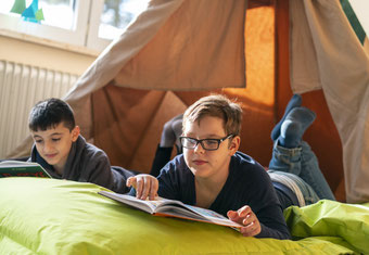 Zwei Kinder lesen in einem selbstgebauten Zelt