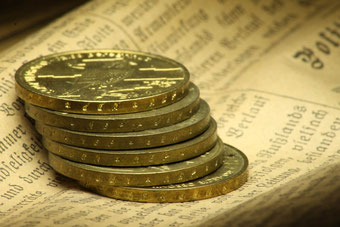 Ein Stapel goldener Münzen auf einer alten Zeitung.