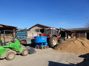 Avant Hoflader im Vordergrund, Traktor mit Betonmischer von de Casê und Frontlader im Hintergrund auf dem Hofgelände eines Pferdehofs