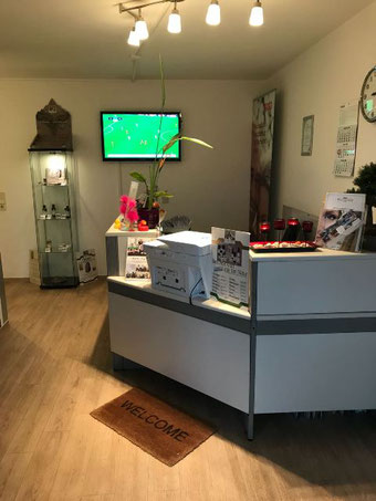 Empfangstresen mit Willkommensmatte, Informationsmaterial und Dekoration in einem Raum mit Holzboden und Fernseher an der Wand