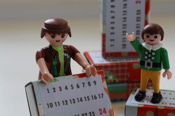 2 Playmobilmännchen halten einen Adventskalendar