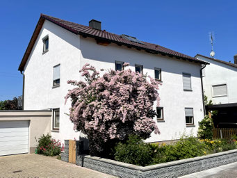 Außenansicht Haus mit der Ferienwohnung FerienNest Kelheim, hellgetönt gestrichen, dunkelrote Dachziegel, großer Strauch im Vorgarten, wunderschön mit Blumen angelegt, daneben Garagenvorplatz