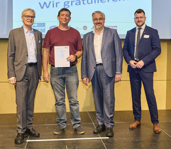 Teilnehmer hält Urkunde neben Gratulanten