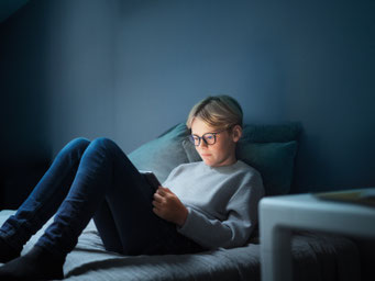 Jugendliche*r liegt auf der Couch und liest im Tablet