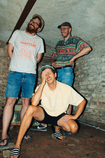Die drei Musiker von Average Pizza in einem Kellergewölbe in Sommerklamotten.