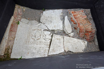 Blick auf den Boden des ehemaligen Mittelschiffs. Es sind die Überreste aus drei Epochen: Rechts ein Fragment eines Pfeilers, in der Mitte zwei zertrümmerte mittelalterliche Grabplatten, links ein Teil eines  Ziegelpflasters aus dem 19. Jh.