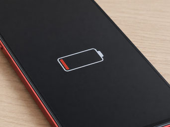 木目のテーブルに置かれたAndroidスマートフォンの画面に、赤い残量表示のバッテリーアイコンが表示されている様子。バッテリーの減りや充電トラブルをイメージしやすい写真。