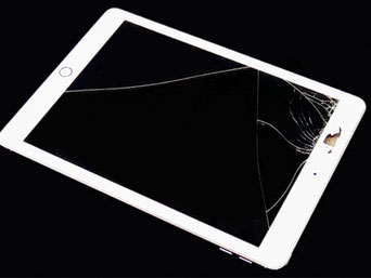 黒い背景の上に置かれた白いiPadの画面表面に、ひび割れとガラス欠けがある写真。iPadのフロントパネルガラス修理や画面割れ修理の症状がわかる状態。