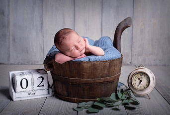 BabyfotografBaby liegt neben Wecker in einem Korb