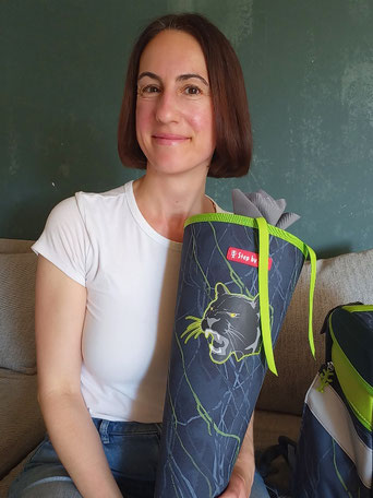 Michaela Dauscher sitzt auf dem Sofa, sie lächelt und hat eine blau-grüne Schultüte in Händen.