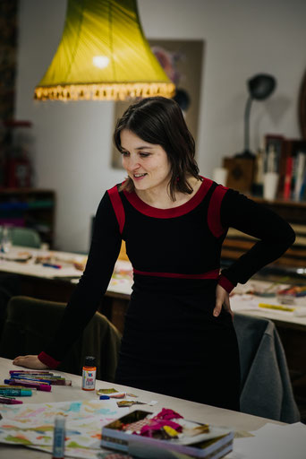 Rebecca Schella Portraitfoto hinter auf dem Tisch stehenden und liegenden Glitzerstiften