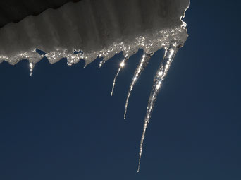 Sonnenstrahlen widerspiegeln sich in Eiszapfen vor stahlblauem Himmel