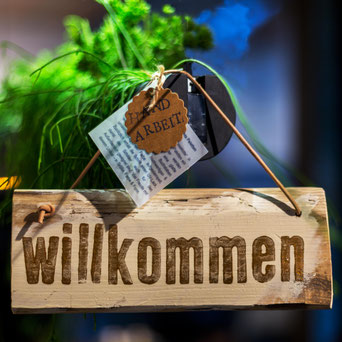Holzschild mit Aufschrift "Willkommen", am Lederband hängend mit einem Etikett "Handarbeit"