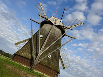 Eine Windmühle vor blauem Himmel mit Schäfchenwolken, leicht schräg fotografiert