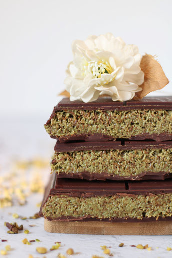 barrettadi cioccolata di Dubai spezzettata e impilata, con fiore bianco all'apice e pioggia di granella di pistacchio sul tavolo