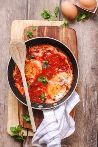 padella con piatto tipico tunisino a base di pomodoro, con cucchiaio in legno, su tagliere