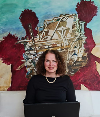 Das Foto zeigt mich vor meinem Kunstwerk "Sogno" (Traum) auf einem weißen Sofa sitzend und ein Laptop auf dem Schoss haltend.