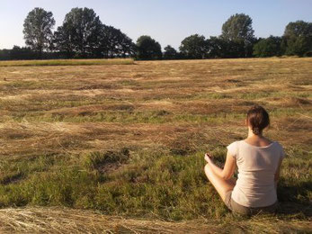 Anika Schlüter sitzt meditierend auf einer Wiese