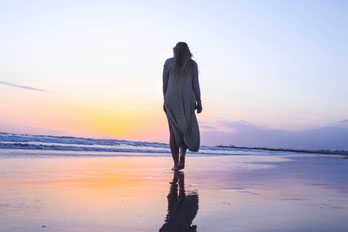 Foto: Frau mit dem Rücken zugewandt geht am Strand in der Abenddämmerung barfuß spazieren