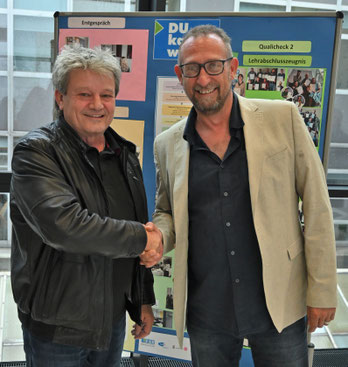 Zwei Männer geben sich vor einer Projektwand freundlich die Hand
