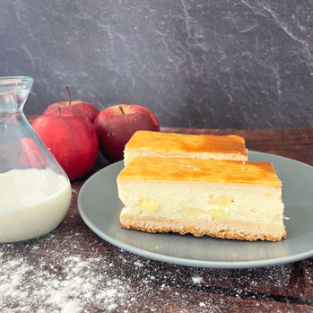 Zwei Stücke Apfel-Schmant-Kuchen auf einem Teller, mit Äpfel und einer Glaskaraffe daneben 