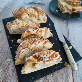 Aufgeschnittener Marzipanstriezel mit Zuckerglasur und Mandelblättchen auf einer schwarzen Schieferplatte, Messer daneben