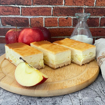 Drei Stück Apfel-Schmand-Kuchen auf einem Brett, daneben frische Äpfel